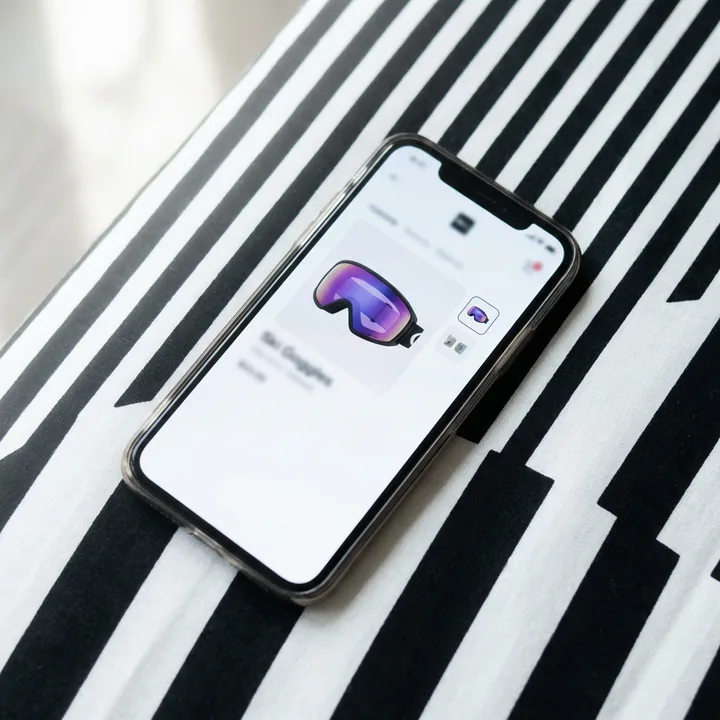 A phone on a black and white striped surface showing a ski goggles product page. Illustration made with AI.